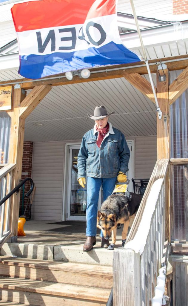Man wearing a cowboy hat reaches out with his foot as his German shepherd guide dog pauses at the top of the stairs
